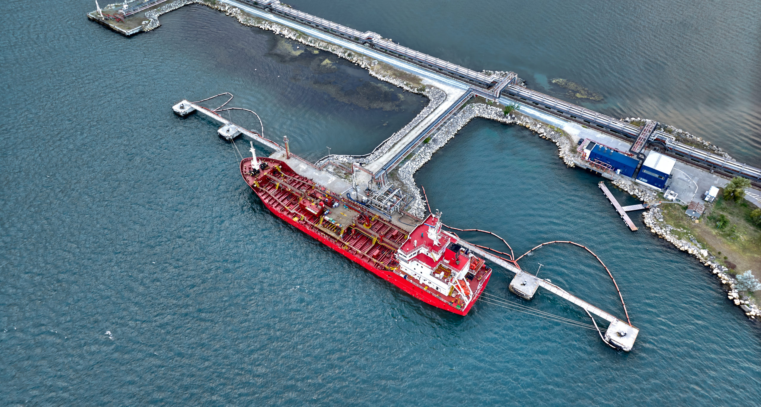 Aerial top view of oil tanker ship at the port, Oil terminal is industrial facility for storage of oil and petrochemical products ready for transport to further storage facilities. Ready for import export business logistic and transportation.